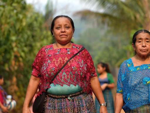 Aurelia, wearing a pink blouse and long skirt, walking to the cenote to collect water. Here she walks with her mother.